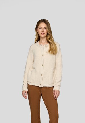 Fuzzy cream cardigan with a round neckline, front button closure, and two pockets. Paired with brown pants, against a neutral background.