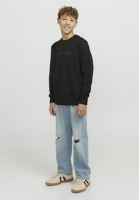 Svart sweatshirt med "ORIGINALS" grafik, ljusblå ripped jeans och beige sneakers med svarta ränder; avslappnad passform och avslappnad stil.