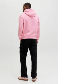 Hoodie rose avec capuche, pantalons cargo noirs et baskets roses. Tissu lisse, coupe décontractée et poches latérales sur les pantalons.