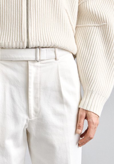 Kreemikattega soonik-sweater, millel on tõmblukk ja sobivad kõrge vöökohaga püksid. Püksid on voltidega ja neil on ristküliku kuju, hõbedane vööklamber.