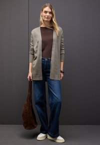 Jasnoszary kardigan, brązowa bluzka, niebieskie szerokie dżinsy, białe trampki oraz brązowa zamszowa torba na ramie. Prosty fason z ribbowanymi akcentami.