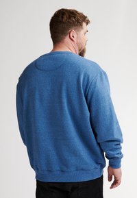 Sudadera azul con tejido texturizado, cuello redondo y puños y dobladillo acanalados. Presenta un detalle de costura circular en la parte posterior.
