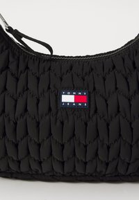 Must mustrilist kott, mis on valmistatud pehmest kangast. Omab silmapaistvat "TOMMY JEANS" logo sildi koos punaste, valgete ja siniste aktsentidega.