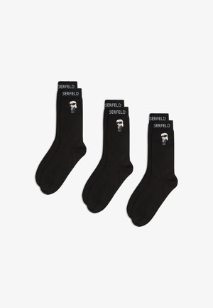 Fekete pamutzokni, amelyen fehér grafika látható napszemüveges alakról a szegélyen, feliratozva: "GERFELD." Három pár kihelyezve.