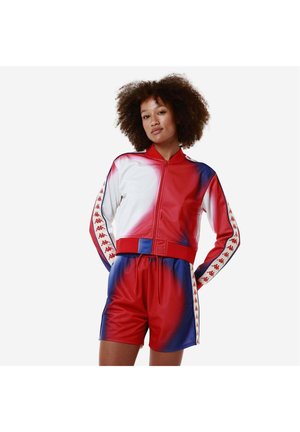 Set sportivo rosso e blu composto da una giacca con zip, pannelli bianchi e dettagli del logo, abbinato a pantaloni corti coordinati con vita elastica.