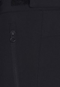 Černá tkanina s kapsou na zip, šitými švy a akcentem na suchý zip. Hladká textura, minimalistický design s funkčními detaily.