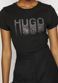 Schwarzes Baumwoll-T-Shirt mit dem Wort "HUGO" in einem Farbverlauf aus silbernen Strasssteinen, kurzen Ärmeln und rundem Ausschnitt.