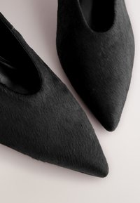 Svarta spetsiga klackskor gjorda av ett texturerat hårliknande material. Snygg design med slät insida och öppna sidor som förhöjer det visuella intrycket.