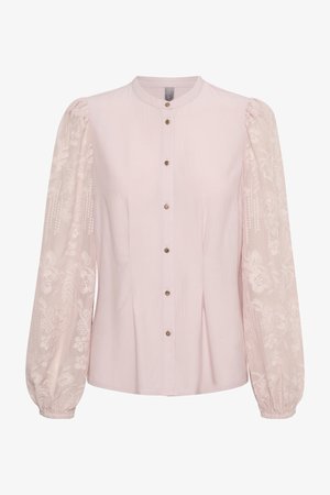 Gaiši rozā blūze ar pogu aizdari priekšā, ar izšūtām caurspīdīgām garām piedurknēm un savelktām aprocēm. Gluda auduma ar ziedu rotājumiem.