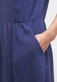 Mörkblå klänning med vita prickar, med elastisk midja, rynkad tyg och en sidogömma. Slät textur.