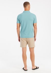 Lichtblauw polo-shirt met korte mouwen, gecombineerd met beige shorts. Het shirt heeft een kraag en een gladde textuur; de shorts hebben een achterzak.