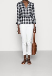 Camisa de cuadros en blanco y negro con peplum, combinada con jeans blancos y un bolso marrón. Sandalias marrones completan el look.