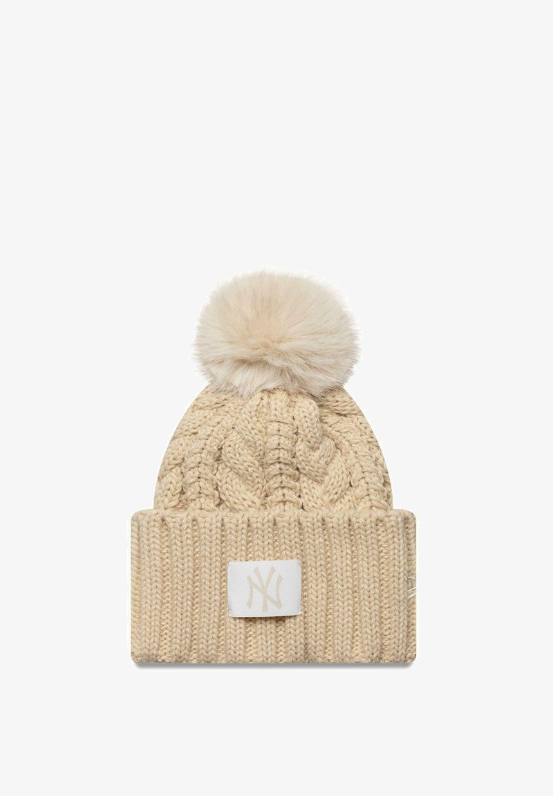 Berretto beige in maglia con un design a trecce testurizzate, risvolto pieghevole e pompon in pelliccia sintetica sulla parte superiore; include una toppa con logo bianco.