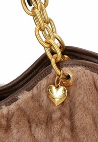 Bolso de piel sintética marrón con correa de cadena dorada. Presenta un charm en forma de corazón con el logo. El detalle muestra una textura suave y un hardware brillante.