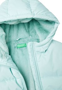 Svetle mátové pufíková bunda s měkkou kožešinovou podšívkou, se stahovací kapucí a zipovým uzávěrem. Štítek nese nápis "United Colors of Benetton."