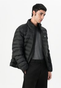 Must kassarõiv tikandiga, kõrge krae ja esiosa tõmblukuga. Omab väikest logo rinnal ja soonikkoes mansette.