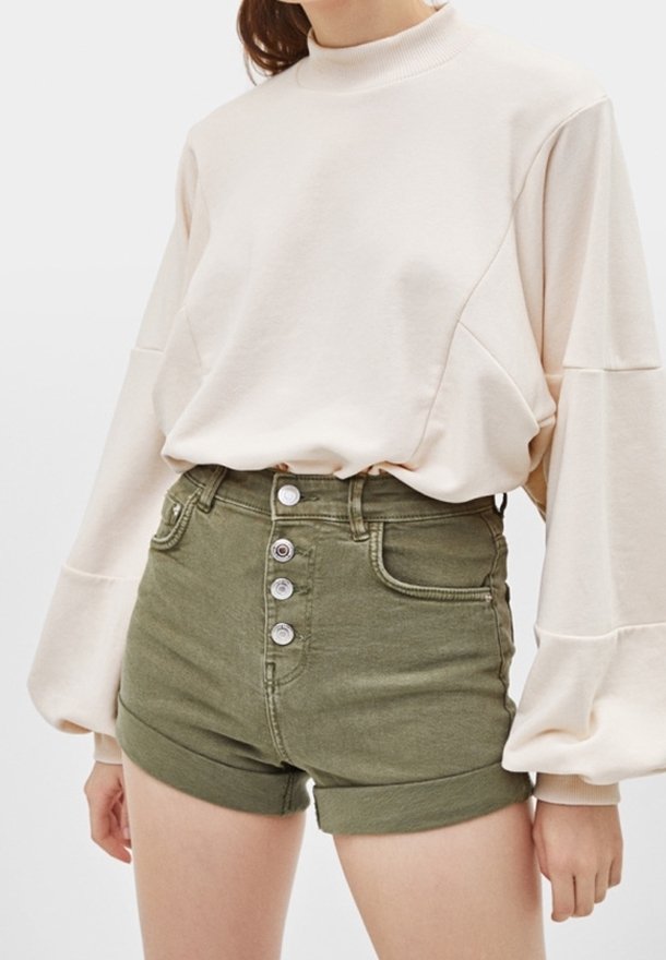Ljusbeige sweatshirt med hög krage, sänkt axel; gröna denimshorts med femknappsstängning och vikta kanter.