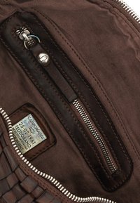 Interni in pelle marrone con texture intrecciata, dotati di una tasca con zip e un'etichetta con dettagli scritti a mano. Fodera in tessuto morbido.