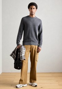 Szary dziany sweter, beżowe spodnie cargo, koszula w kratę zarzucona, czarna torba i szaro-białe sneakersy. Gładkie faktury w swobodnym stylu.