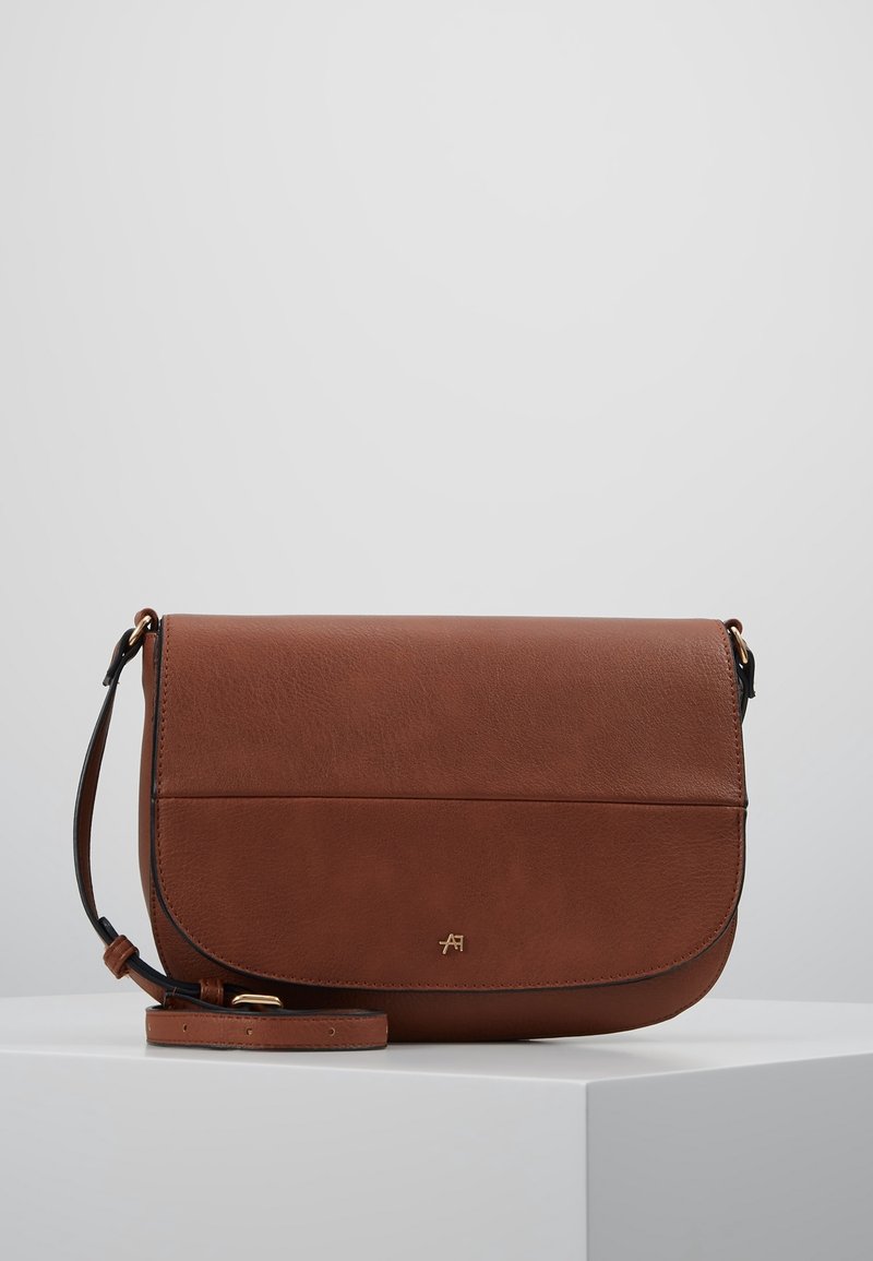 Hnědá kožená krosbody taška s klopou, hladkým povrchem a zlatými akcenty. Obsahuje nastavitelné ramenní popruhy pro pohodlné nošení.