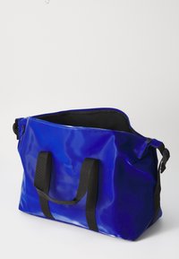 Blue waterproof duffle bag with black webbing handles, smooth texture, and a zipper closure, featuring an interior black lining.
