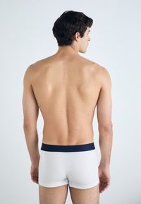 White boxer briefs with a dark navy waistband, shown from the back on a bare torso against a neutral background. Smooth fabric texture.