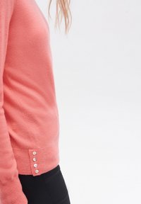 Różowy sweter wykonany z miękkiego materiału. Dopasowany krój z prążkowym dołem i pięcioma dekoracyjnymi guzikami po boku.