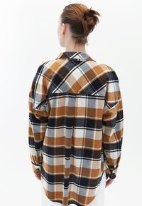 Camisa de franela a cuadros en marrón y azul marino, con mangas largas, puños abotonados y un cuello clásico. Textura suave y un ajuste relajado.