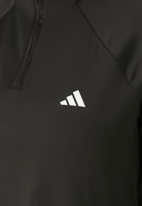 Pullover sportivo nero con colletto alto, realizzato in tessuto morbido. Presenta un logo triangolare bianco sul lato sinistro.