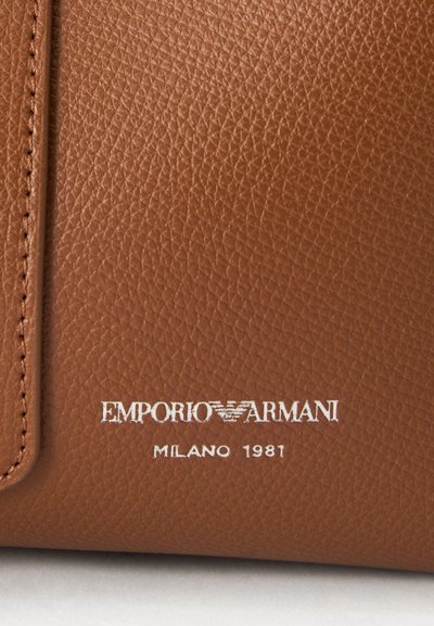 Καφέ υφή δέρματος με λευκό λογότυπο Emporio Armani και ανάγλυφο κείμενο Milano 1981 κοντά στην ραμμένη άκρη.