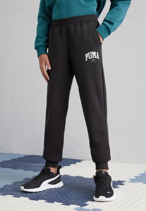 Pantalones deportivos negros con una cinturilla acanalada y bolsillos laterales; presenta un logo blanco de Puma en el muslo izquierdo. Usados con zapatillas deportivas negras.