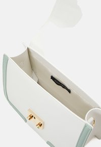 Bílá kožená kabelka s mátově zelenými akcenty. Má zlaté zapínání na sponu a vnitřní kapsu s označením. Hladká textura, obdélníkový tvar.