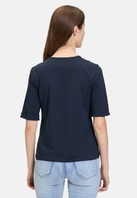Granatowy bawełniany t-shirt z podwiniętymi krótkimi rękawami, okrągłym dekoltem i luźnym krojem, w połączeniu z jasnoniebieskimi dżinsami.