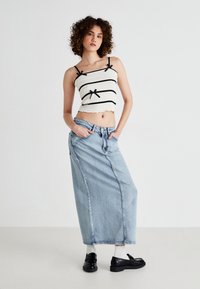 White smocked crop top with black stripes and bows, paired with a long light blue denim skirt. Black shoes complete the outfit.