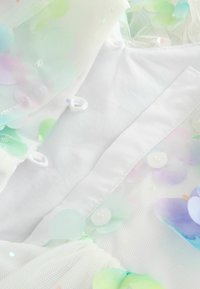 Valge kangas, millel on kihiline võrk ja pastelsel toonis lillekujulised litrid rohelises, roosas ja sinises. Kinnitatud väikeste valgete nööpidega.