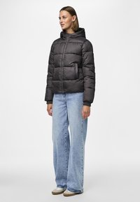 Vadderad jacka i mörkgrått med dragkedja framtill, huva och elastiska ärmslut. Bärs med ljusblå vida jeans och beiga skor.