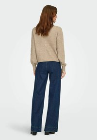 Beżowy sweter dzianinowy o prążkowanej fakturze, w połączeniu z ciemnoniebieskimi jeansami o szerokim kroju z akcentowanym dołem. Model pokazany z tyłu.