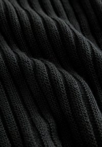 Primo piano di un tessuto nero a coste lavorato a maglia, con morbide pieghe e strisce verticali texture.