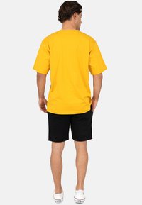 T-shirt jaune à manches courtes avec col rond, associé à un short noir. La tenue présente une coupe décontractée et un style casual.