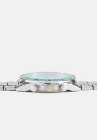 Montre en acier inoxydable argenté avec une lunette bleu clair, un cadran en verre rond, trois boutons-poussoirs et un bracelet en métal à maillons.