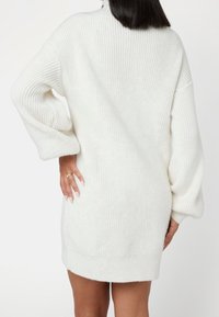Vestito a maglia bianco con texture a coste, maniche oversize e silhouette dritta. Presenta spacchi laterali e un aspetto morbido e accogliente.