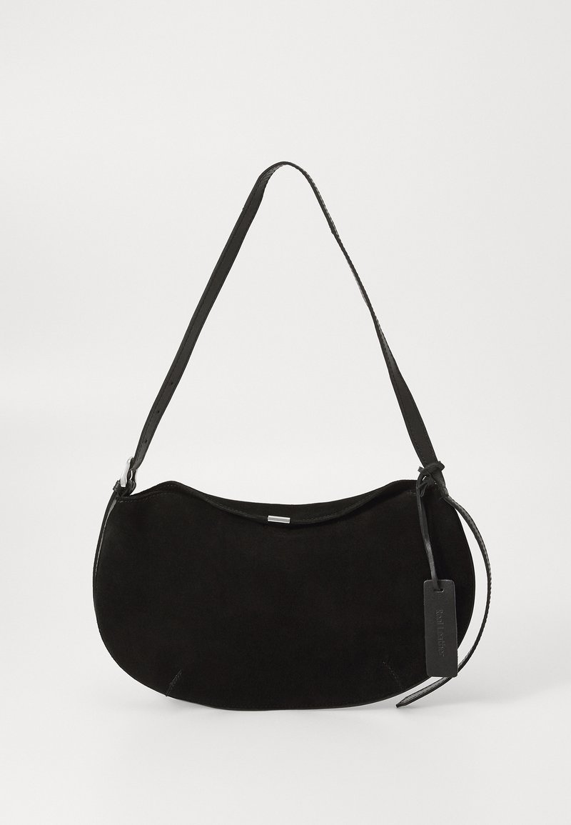 Sac à épaule en daim noir avec une forme incurvée, une bandoulière réglable et une étiquette en cuir suspendue d'un côté.
