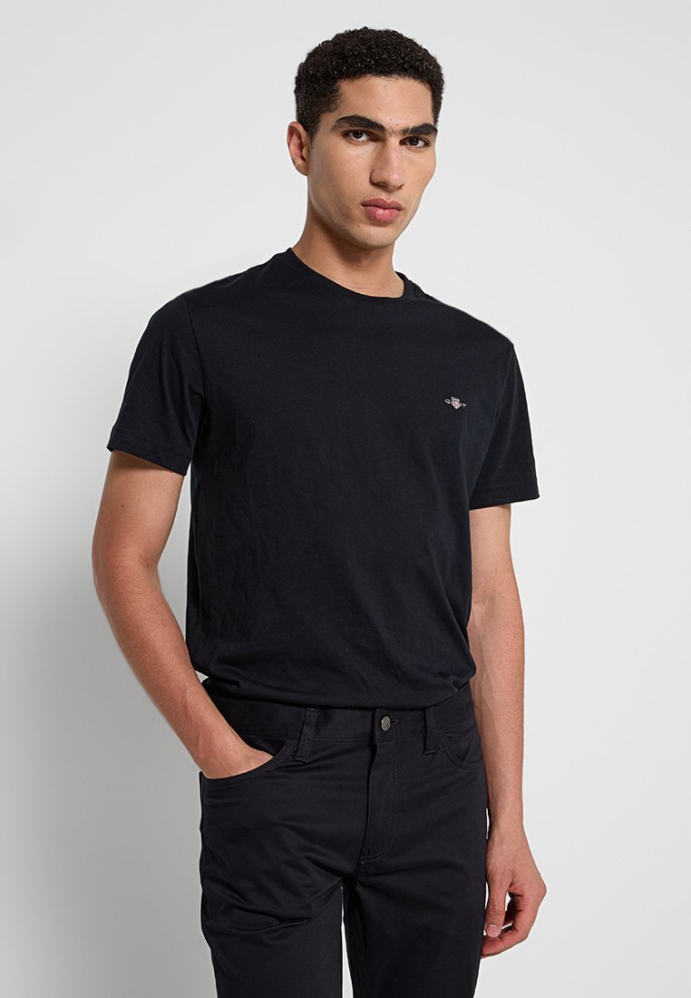 Czarny bawełniany t-shirt z okrągłym dekoltem, krótkimi rękawami i małym logo na lewej piersi. Gładka tekstura, luźny krój.