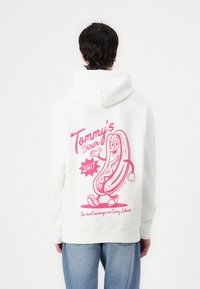 Witte hoodie met een cartoon hotdog afbeelding in het roze op de achterkant. Tekst luidt "Tommy's Diner 24/7" en "De beste worst op Coney Island."