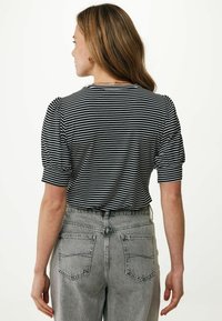 Top a maniche corte a righe bianche e nere con spalle a sbuffo, abbinato a jeans grigi chiari a vita alta. Sfondo semplice.