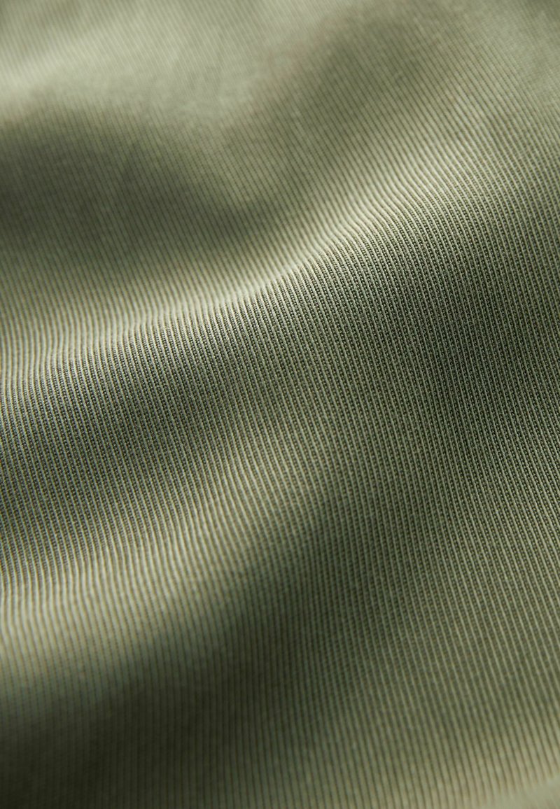 Tissu texturé en vert muted avec de fines rayures verticales, présentant une surface lisse et un subtil éclat, créant une apparence structurée.
