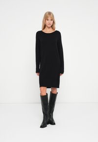 Abito maglione nero a maglia con scollatura arrotondata e maniche lunghe, caratterizzato da polsini a coste e una vestibilità comoda; abbinato a stivali neri al ginocchio.