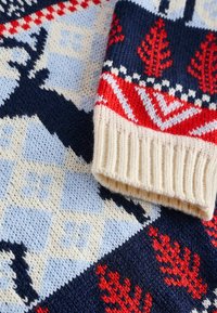 Sweter wykonany na drutach, z geometrycznym wzorem w odcieniach granatu, czerwieni, kremu i jasnoniebieskiego, z prążkowanymi mankietami i fakturowanymi elementami wzorniczymi.