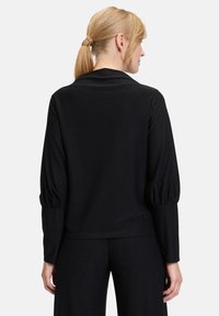 Schwarzes Langarm-Top mit rundem Ausschnitt, strukturiertem Stoff und Puffärmeln. Getragen mit passenden schwarzen Hosen, die eine schlanke Silhouette zeigen.
