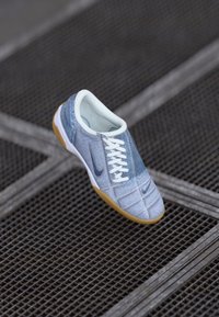 Světle modré denimové tenisky s bílými tkaničkami a tmavě modrými akcenty, s kulatou špičkou a gumovou podrážkou. Texturovaný povrch s detaily šití.